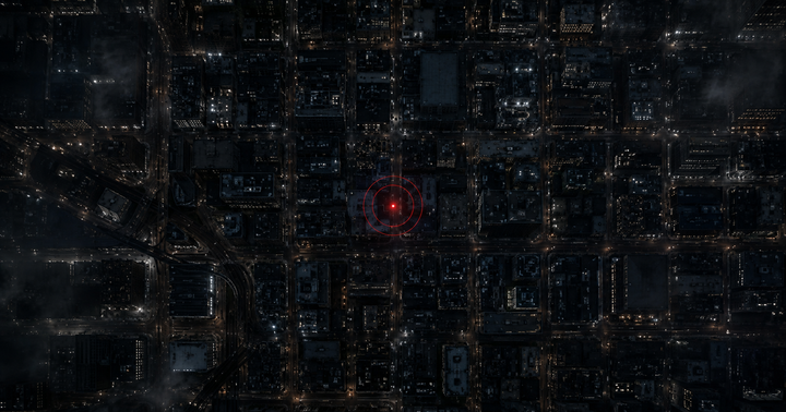 Aerial nighttime view of a city grid, seen from above as if from a surveillance drone